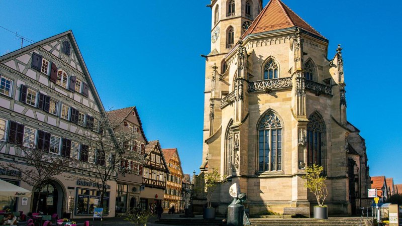 Die Stadtkirche in Schorndorf mit ihrem markanten Turm steht neben traditionellen Fachwerkh&auml;usern unter einem klaren blauen Himmel., &copy; Stuttgart-Marketing GmbH, Sarah Schmid
