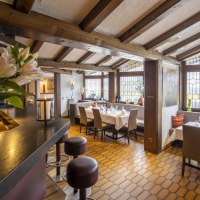 Ein gemütliches Restaurant mit Holzbalkendecke, gedeckten Tischen und großen Fenstern. Blumen und Kerzen sorgen für eine einladende Atmosphäre., © Hotel Gloria GmbH Ein gemütliches Restaurant mit Holzbalkendecke, gedeckten Tischen und großen Fenstern. Blumen und Kerzen sorgen für eine einladende Atmosphäre., © Hotel Gloria GmbH