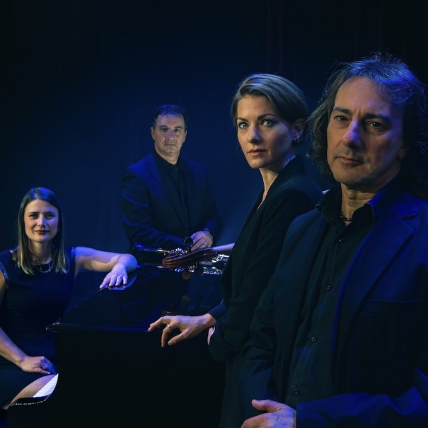 Vier Musiker in dunkler Kleidung posieren ernst vor einem dunklen Hintergrund. Sie stehen um ein Klavier herum., &copy; Buchhandlung Im Roten Haus