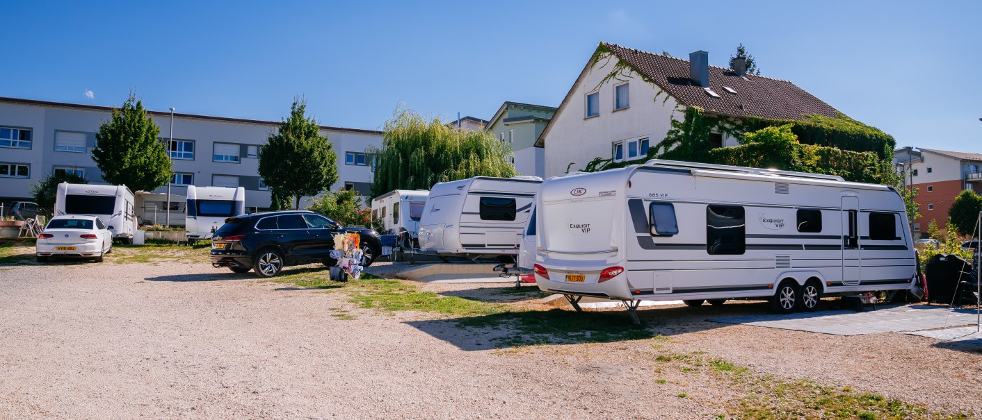 Wohnmobilstellplatz mit Wohnwagen und Autos, umgeben von Gebäuden und Bäumen unter klarem Himmel., © Stuttgart-Marketing GmbH, Thomas Niedermüller