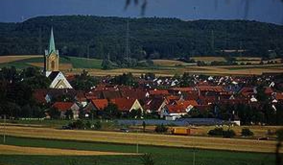Ein Dorf mit roten Dächern und einer Kirche mit grünem Turm, umgeben von Feldern und Hügeln im Hintergrund., © http://www.renningen.de/index.php?id=574