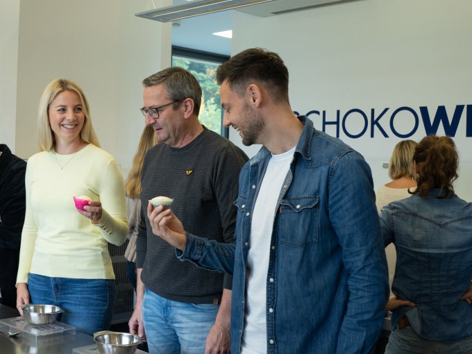 Mehrere Personen stehen in einem Raum, halten Schokolade und lächeln. Im Hintergrund ist ein Schild mit der Aufschrift 'SCHOKO' sichtbar., © Alfred Ritter GmbH & Co. KG | Waldenbuch Mehrere Personen stehen in einem Raum, halten Schokolade und lächeln. Im Hintergrund ist ein Schild mit der Aufschrift 'SCHOKO' sichtbar., © Alfred Ritter GmbH & Co. KG | Waldenbuch