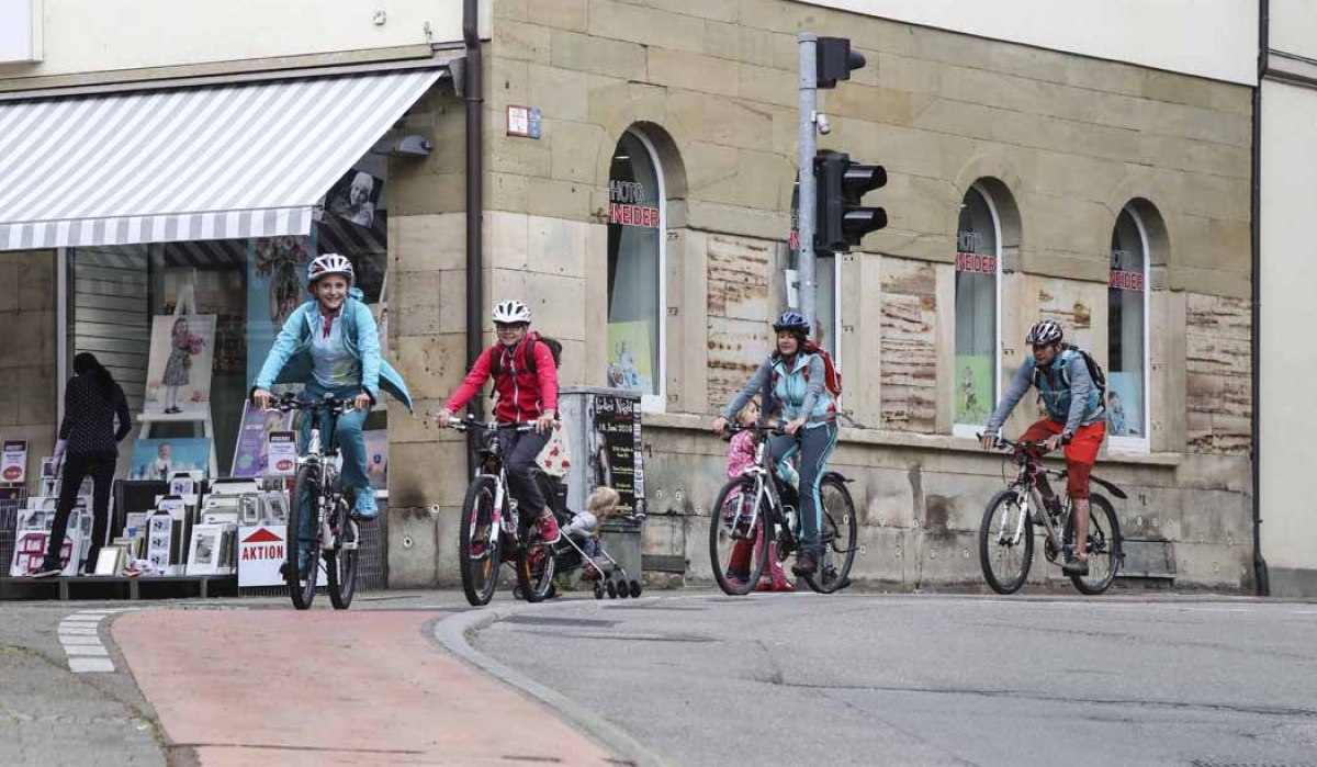 Eine Gruppe von Radfahrern, darunter Kinder, fährt durch die Kirchheimer Innenstadt. Sie tragen Helme und sind auf einem Radweg unterwegs., © Schwäbische Alb Tourismusverband e.V. Eine Gruppe von Radfahrern, darunter Kinder, fährt durch die Kirchheimer Innenstadt. Sie tragen Helme und sind auf einem Radweg unterwegs., © Schwäbische Alb Tourismusverband e.V.
