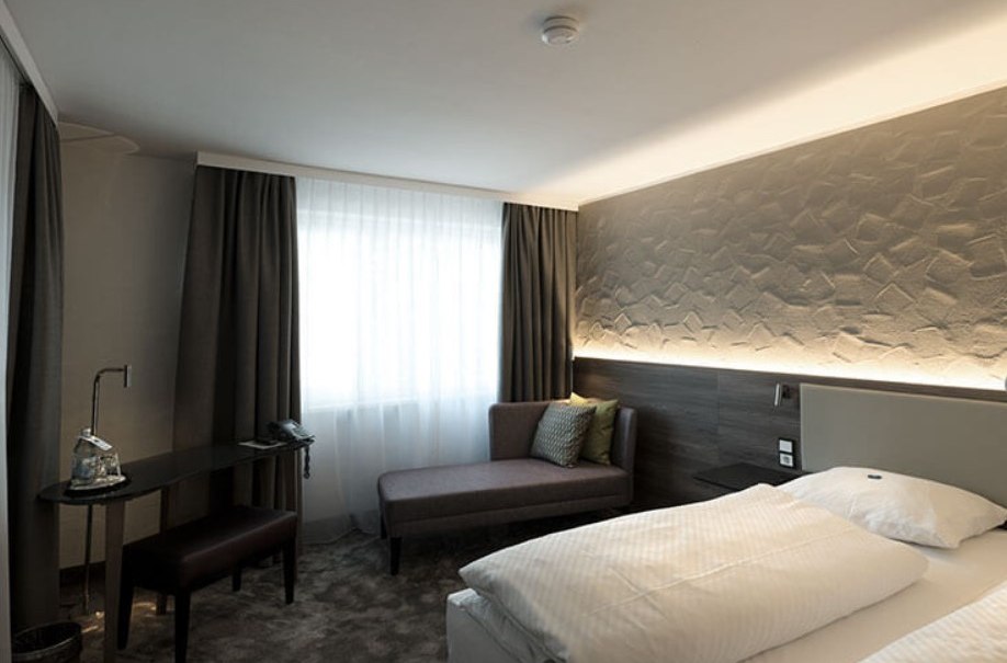 Modernes Hotelzimmer mit Doppelbett, Sofa, Schreibtisch und stilvoller Beleuchtung. Neutrale Farben und gem&uuml;tliche Atmosph&auml;re., &copy; Hotel am Park