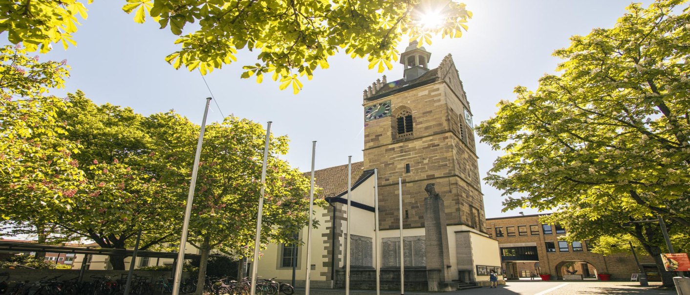 Die Lutherkirche in Fellbach mit ihrem markanten Turm, umgeben von grünen Bäumen und Sonnenschein, bietet einen idyllischen Anblick., © SMG, Sarah Schmid