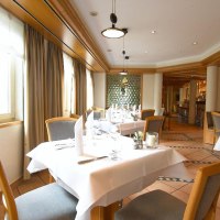 Ein elegantes Restaurant mit weißen Tischdecken, Holzstühlen und großen Fenstern. Die Einrichtung ist modern mit warmen Holztönen., © Hotel am Park