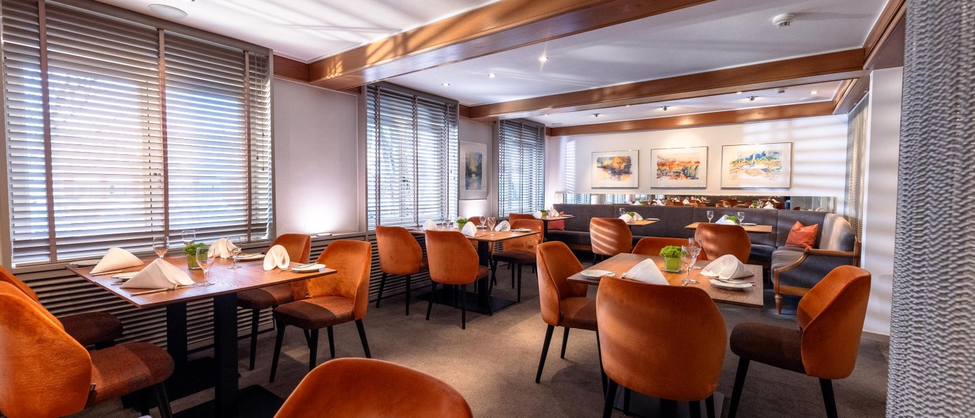 Elegantes Restaurant mit orangefarbenen Stühlen, gedeckten Tischen und Kunst an den Wänden. Große Fenster mit Jalousien lassen Licht herein., © Ringhotel Adler Asperg