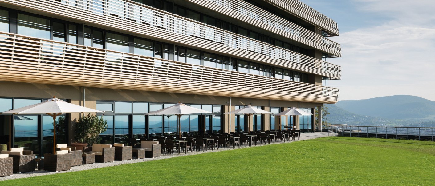 Modernes Hotel mit großen Fenstern, Terrasse mit Sonnenschirmen und grüner Wiese im Vordergrund, blauer Himmel im Hintergrund., © Achalm. Hotel GmbH & Co. KG Modernes Hotel mit großen Fenstern, Terrasse mit Sonnenschirmen und grüner Wiese im Vordergrund, blauer Himmel im Hintergrund., © Achalm. Hotel GmbH & Co. KG