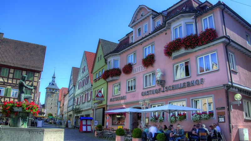 Hotel Schillerhof in einer malerischen Altstadt mit Fachwerkhäusern, einem Brunnen und Menschen, die im Freien sitzen. Sonniges Wetter und blauer Himmel., © Hotel Schillerhof Hotel Schillerhof in einer malerischen Altstadt mit Fachwerkhäusern, einem Brunnen und Menschen, die im Freien sitzen. Sonniges Wetter und blauer Himmel., © Hotel Schillerhof