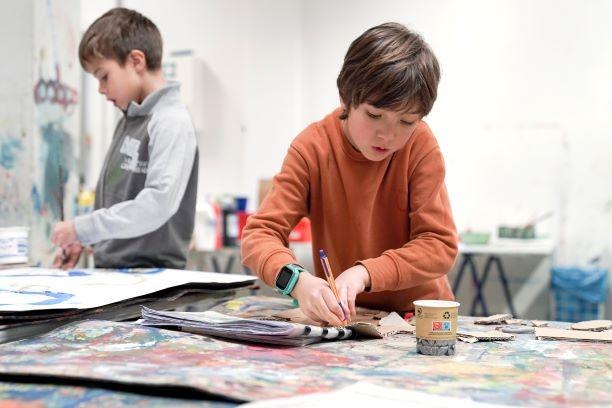 Zwei Kinder sind in einem Kunstworkshop vertieft. Sie arbeiten an einem Tisch mit verschiedenen Materialien und Farben., &copy; Kunstschule Labyrinth