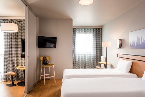 Modernes Hotelzimmer mit zwei Einzelbetten, Fernseher, Tisch und Stuhl. Ein Vorhang trennt den Schlafbereich vom Sitzbereich., © adagio access Stuttgart Airport Messe
