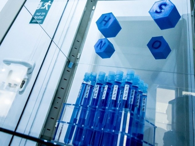 Blau beleuchtete Reagenzgläser in einem Regal, darüber chemische Symbole H, N, S, O. Notausgangsschild im Hintergrund., © ExitGames Stuttgart Blau beleuchtete Reagenzgläser in einem Regal, darüber chemische Symbole H, N, S, O. Notausgangsschild im Hintergrund., © ExitGames Stuttgart