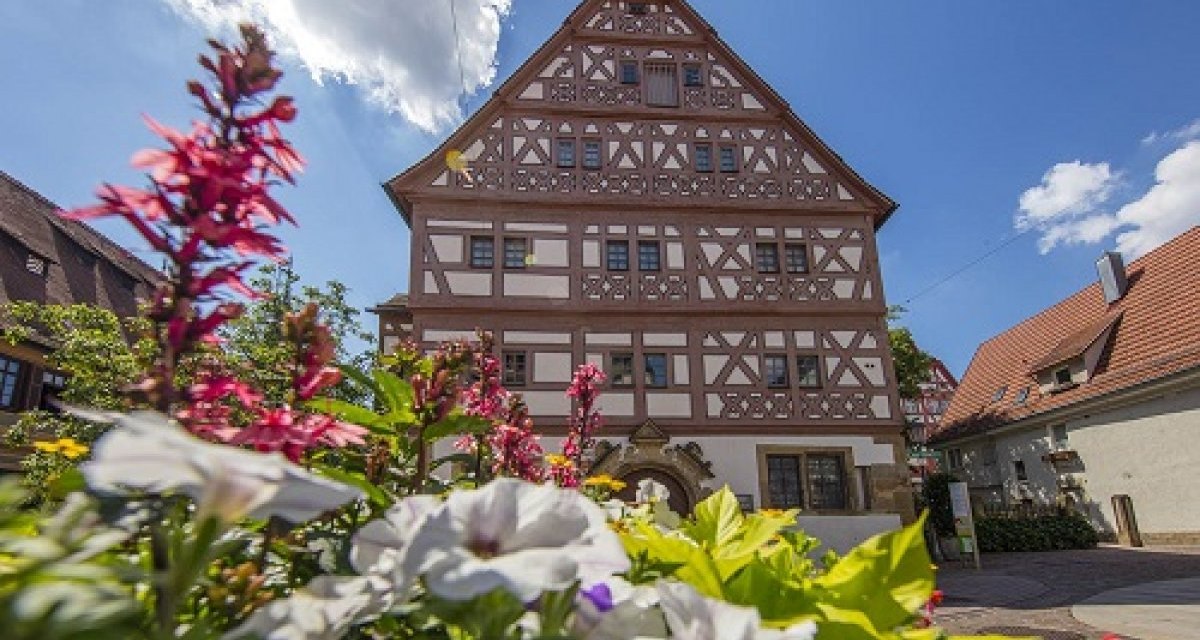 Fachwerkhaus mit reich verziertem Giebel, umgeben von bl&uuml;henden Blumen im Vordergrund. Der Himmel ist blau mit einigen Wolken., &copy; Achim Mende