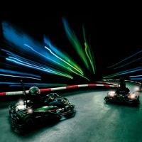 Zwei Karts fahren auf einer beleuchteten Indoor-Strecke. Lichtstreifen in Blau und Grün erzeugen einen dynamischen Effekt., © Sensapolis Sindelfingen