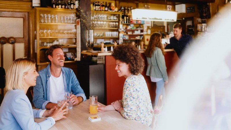Drei Personen sitzen lachend an einem Tisch in einer gemütlichen Bar. Im Hintergrund sind Gläser und Flaschen zu sehen., © Stuttgart-Marketing GmbH, Alwin Maigler Drei Personen sitzen lachend an einem Tisch in einer gemütlichen Bar. Im Hintergrund sind Gläser und Flaschen zu sehen., © Stuttgart-Marketing GmbH, Alwin Maigler