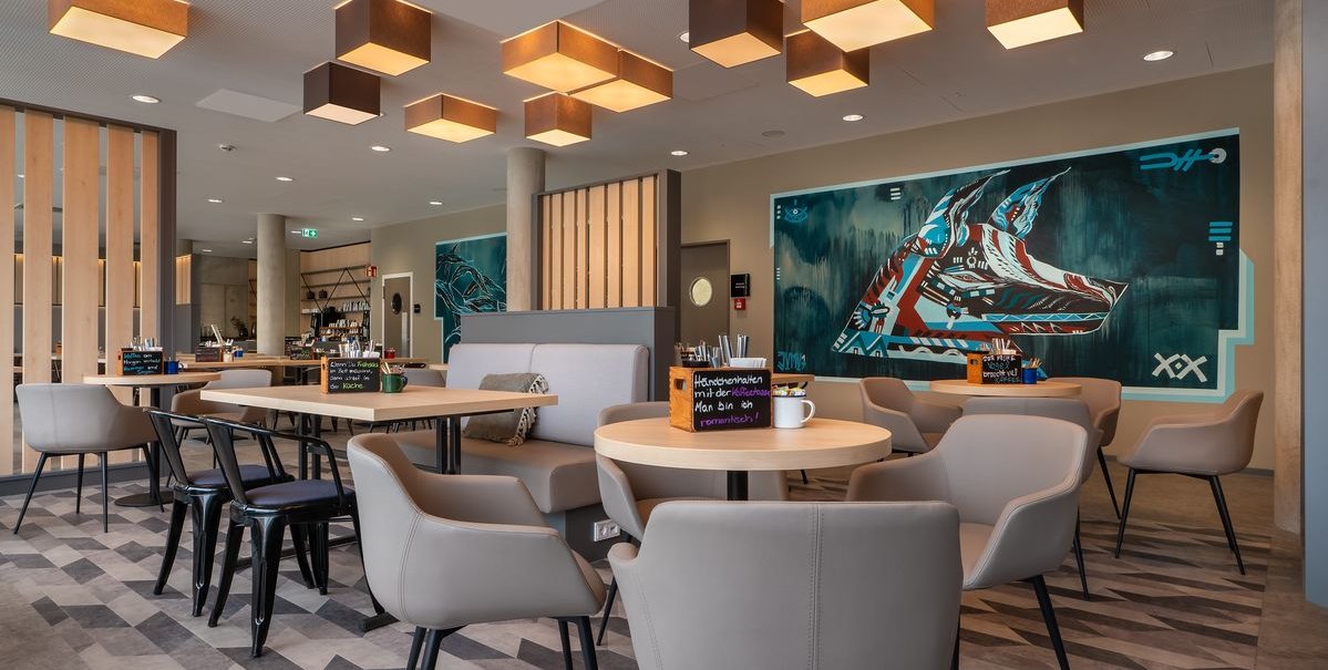 Modernes Restaurant mit stilvollen Möbeln, geometrischen Deckenleuchten und Wandkunst. Runde Tische und bequeme Stühle schaffen eine einladende Atmosphäre., © Novum Hospitality Modernes Restaurant mit stilvollen Möbeln, geometrischen Deckenleuchten und Wandkunst. Runde Tische und bequeme Stühle schaffen eine einladende Atmosphäre., © Novum Hospitality