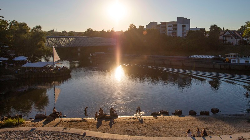 Sonnenuntergang am Neckarstrand in Remseck. Menschen entspannen am sandigen Ufer, während ein Schiff den Fluss passiert. Die Sonne spiegelt sich im Wasser., © Stuttgart-Marketing GmbH, Achim Mende