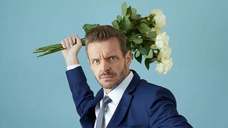 Ein Mann in einem blauen Anzug posiert dramatisch mit einem Strau&szlig; wei&szlig;er Rosen vor einem blauen Hintergrund., &copy; Konzertkreis Triangel Compagnia Compostelli e.V.