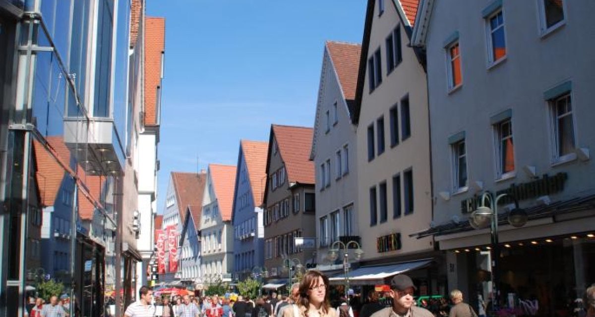 Belebte Einkaufsstraße in Reutlingen mit historischen Giebelhäusern und modernen Glasfassaden. Menschen flanieren bei sonnigem Wetter., © Mythos Schwäbische Alb im Landkreis Reutlingen e.V. Belebte Einkaufsstraße in Reutlingen mit historischen Giebelhäusern und modernen Glasfassaden. Menschen flanieren bei sonnigem Wetter., © Mythos Schwäbische Alb im Landkreis Reutlingen e.V.