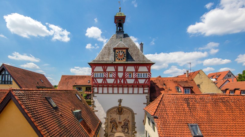 Fachwerkgebäude mit Uhrturm in Bietigheim-Bissingen, umgeben von roten Ziegeldächern und blauem Himmel., © SMG, Achim Mende Fachwerkgebäude mit Uhrturm in Bietigheim-Bissingen, umgeben von roten Ziegeldächern und blauem Himmel., © SMG, Achim Mende