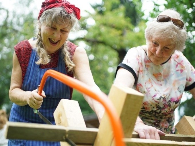 Zwei ältere Frauen sägen gemeinsam Holz im Freien. Sie wirken fröhlich und konzentriert. Eine trägt ein Kopftuch, die andere eine Sonnenbrille., © Cool-Tours StattReisen Zwei ältere Frauen sägen gemeinsam Holz im Freien. Sie wirken fröhlich und konzentriert. Eine trägt ein Kopftuch, die andere eine Sonnenbrille., © Cool-Tours StattReisen