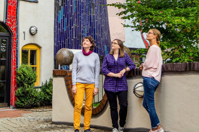 Drei Frauen stehen vor einem farbenfrohen Gebäude im Hundertwasser-Stil in Plochingen. Sie schauen nach oben und wirken interessiert., © PlochingenInfo Drei Frauen stehen vor einem farbenfrohen Gebäude im Hundertwasser-Stil in Plochingen. Sie schauen nach oben und wirken interessiert., © PlochingenInfo