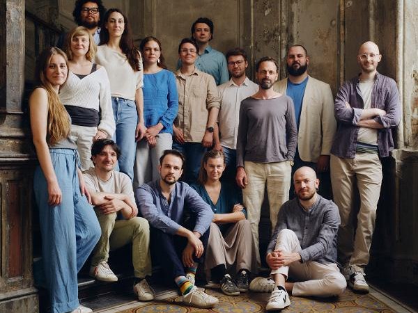 Eine Gruppe von 15 Personen posiert in einem alten Gebäude mit kunstvollen Fliesen und abgenutzten Wänden., © Backnang Eine Gruppe von 15 Personen posiert in einem alten Gebäude mit kunstvollen Fliesen und abgenutzten Wänden., © Backnang