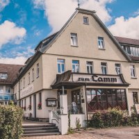 Ein traditionelles Gasthaus mit der Aufschrift 'zum Lamm', umgeben von blühenden Sträuchern und unter einem blauen Himmel mit weißen Wolken., © Stadt Welzheim