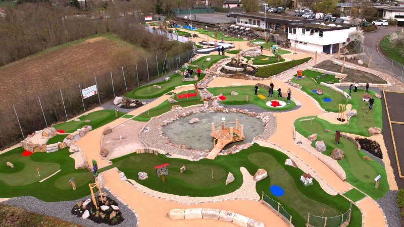 Luftaufnahme eines Adventure-Golfplatzes in Vaihingen mit gr&uuml;nen Bahnen, Hindernissen und einem zentralen Teich. Menschen spielen auf dem Platz., &copy; TV Vaihingen/Enz