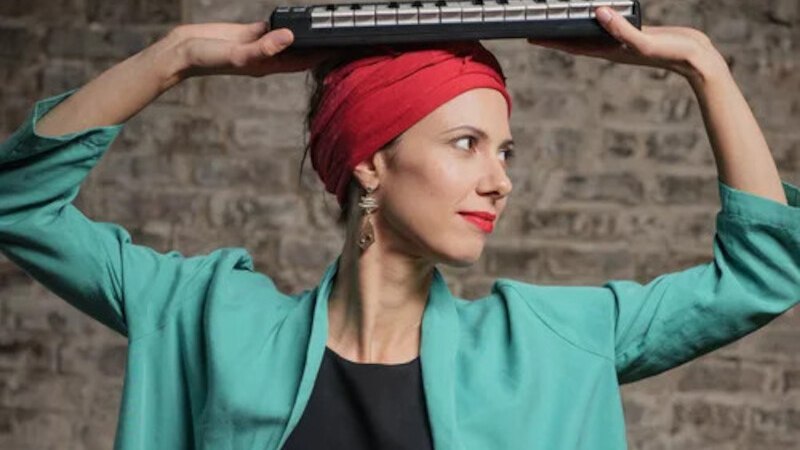 Frau mit rotem Turban und türkisem Mantel hält ein kleines Keyboard über ihrem Kopf vor einer Backsteinwand., © Jazzclub Schwäbisch Hall e.V.