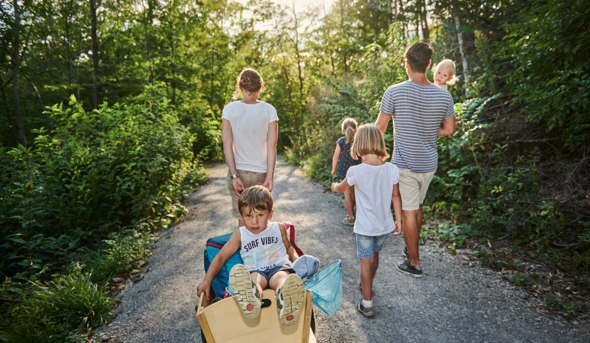 Familie spaziert auf einem Waldweg. Ein Kind sitzt in einem Wagen, während die anderen gehen. Die Sonne scheint durch die Bäume., © Natur.Nah. Schönbuch & Heckengäu Familie spaziert auf einem Waldweg. Ein Kind sitzt in einem Wagen, während die anderen gehen. Die Sonne scheint durch die Bäume., © Natur.Nah. Schönbuch & Heckengäu