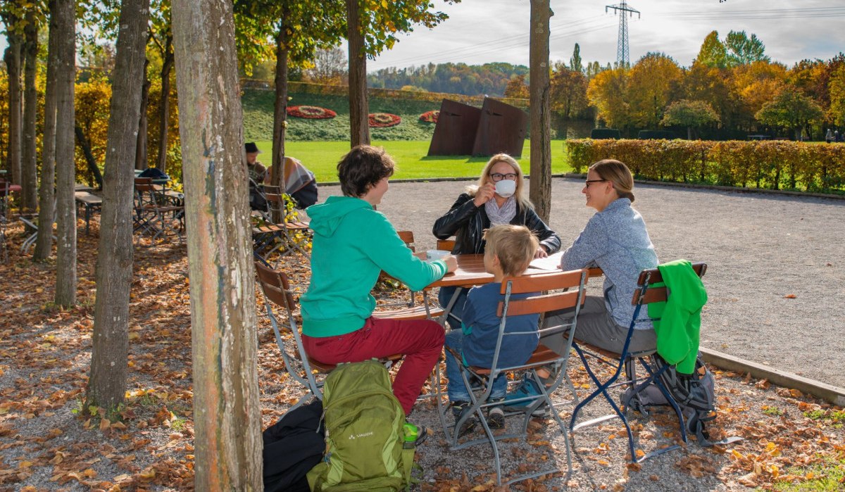 Menschen sitzen im Biergarten Steiner am Fluss, umgeben von Bäumen und Herbstlaub, bei sonnigem Wetter., © Bildergalerie Attila Menschen sitzen im Biergarten Steiner am Fluss, umgeben von Bäumen und Herbstlaub, bei sonnigem Wetter., © Bildergalerie Attila