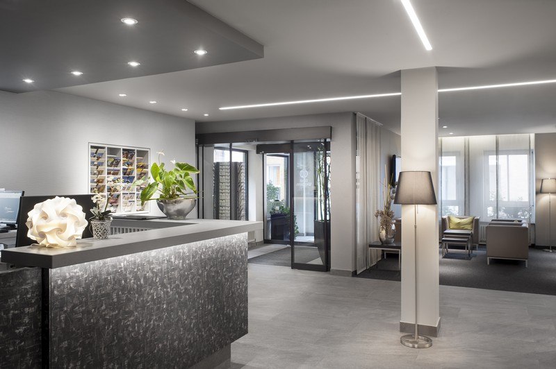 Moderne Hotelrezeption mit stilvollem Schreibtisch, Pflanzen und einem einladenden Sitzbereich im Hintergrund., © TOMAS