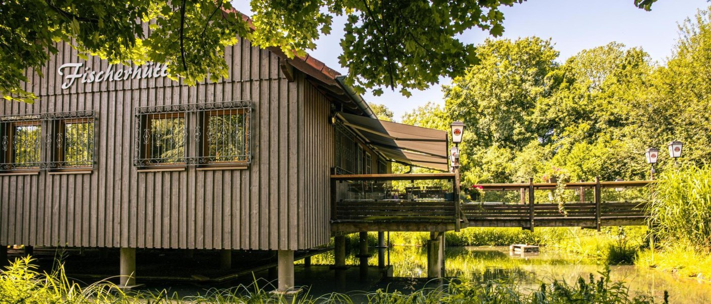 Die Fischerhütte in Plochingen steht auf Stelzen über einem Teich. Eine Terrasse mit Sonnenschutz lädt zum Verweilen ein, umgeben von grüner Natur., © Stuttgart-Marketing GmbH, Sarah Schmid Die Fischerhütte in Plochingen steht auf Stelzen über einem Teich. Eine Terrasse mit Sonnenschutz lädt zum Verweilen ein, umgeben von grüner Natur., © Stuttgart-Marketing GmbH, Sarah Schmid