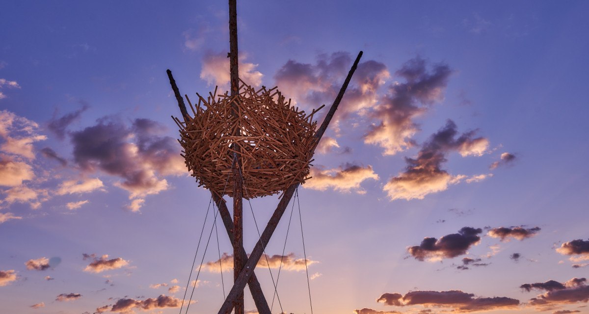 Eine gro&szlig;e Vogelnest-Skulptur aus Holz thront vor einem dramatischen Sonnenuntergang mit violettem Himmel und Wolken., &copy; Natur.Nah. Sch&ouml;nbuch & Heckeng&auml;u