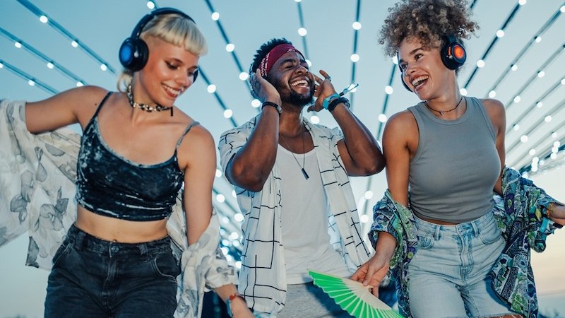 Drei Personen tanzen fr&ouml;hlich mit Kopfh&ouml;rern bei einer Silent Disco unter leuchtenden Lichterketten., &copy; EMT Event-Media-Tec GmbH