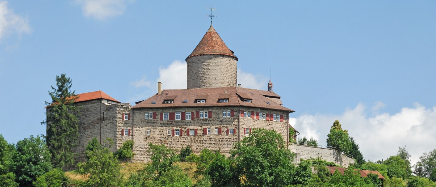 Burg Reichenberg in Oppenweiler, umgeben von grünen Bäumen und blauem Himmel. Der runde Turm und das Hauptgebäude sind aus Stein mit roten Dächern., © FVG Schwäbischer Wald Burg Reichenberg in Oppenweiler, umgeben von grünen Bäumen und blauem Himmel. Der runde Turm und das Hauptgebäude sind aus Stein mit roten Dächern., © FVG Schwäbischer Wald