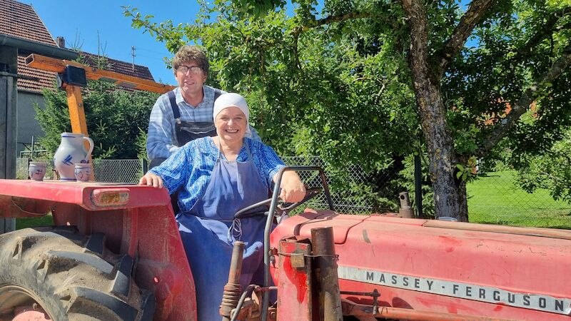 Zwei Personen auf einem roten Massey Ferguson Traktor. Eine Person sitzt am Steuer, die andere steht dahinter. Im Hintergrund sind Bäume und ein Haus., © NPG Messe und Veranstaltungs-GmbH Zwei Personen auf einem roten Massey Ferguson Traktor. Eine Person sitzt am Steuer, die andere steht dahinter. Im Hintergrund sind Bäume und ein Haus., © NPG Messe und Veranstaltungs-GmbH