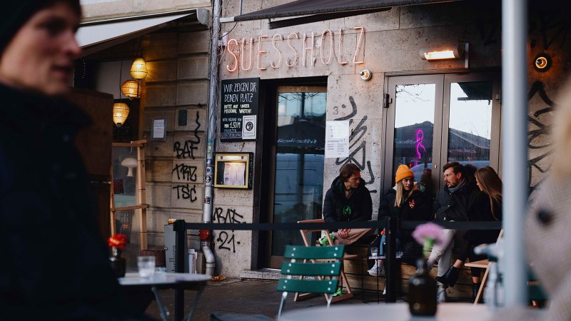 Au&szlig;enansicht des Caf&eacute;s 'Suessholz' im Leonhardsviertel. Menschen sitzen drau&szlig;en, unterhalten sich. Graffiti an den W&auml;nden, Neonlicht im Fenster., &copy; Stuttgart-Marketing GmbH, Alwin Maigler
