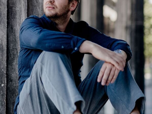 Ein Mann in einem blauen Hemd und grauer Hose sitzt nachdenklich auf einer Steinbank., &copy; Kulturforum Schorndorf e. V.