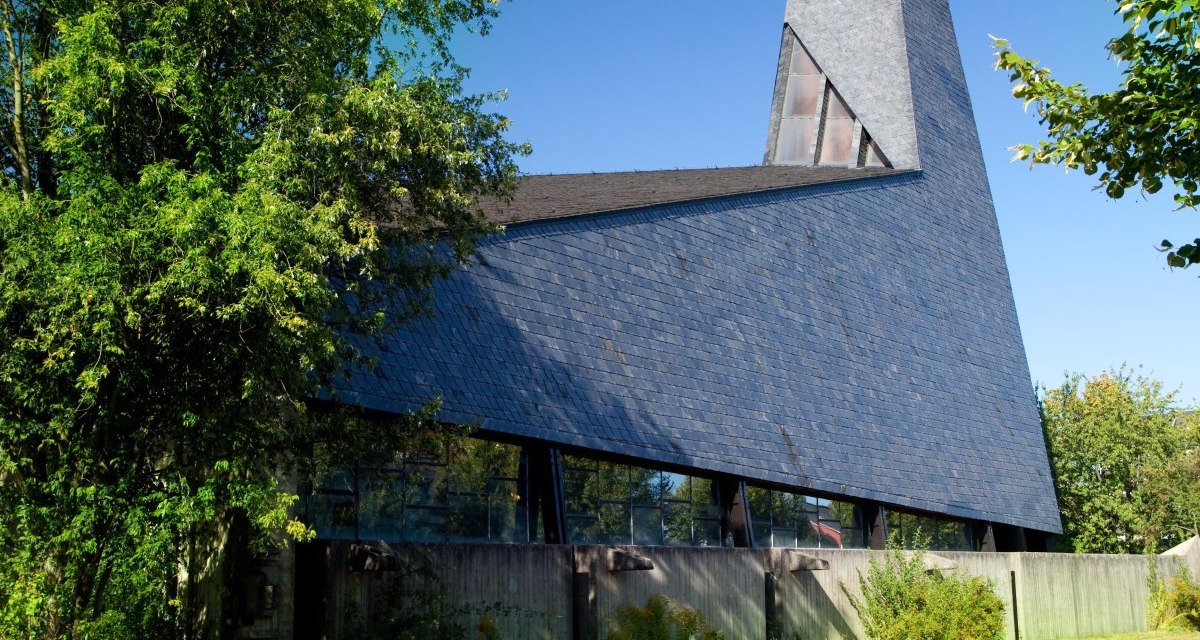 Moderne Kirche mit spitzem Turm und Schieferdach, umgeben von Bäumen und Rasenfläche, unter klarem blauem Himmel., © Waiblingen - Stuttgart-Marketing GmbH Moderne Kirche mit spitzem Turm und Schieferdach, umgeben von Bäumen und Rasenfläche, unter klarem blauem Himmel., © Waiblingen - Stuttgart-Marketing GmbH