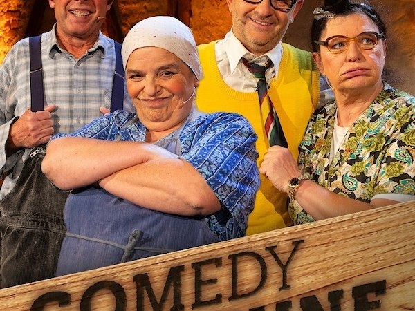 Vier Personen in lustigen Kost&uuml;men posieren vor einem Schild mit der Aufschrift 'Comedy Scheune'. Sie tragen Brillen und M&uuml;tzen., &copy; NPG Messe und Veranstaltungs-GmbH