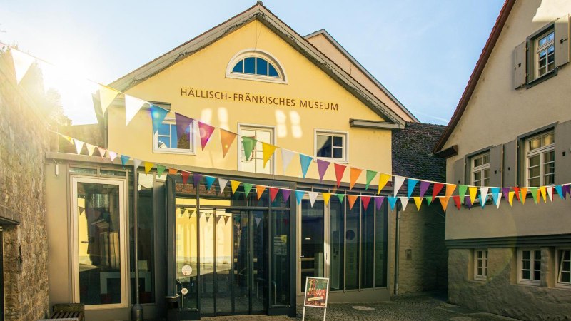 Das Hällisch-Fränkische Museum in Schwäbisch Hall, geschmückt mit bunten Wimpeln unter strahlendem Sonnenschein., © Stuttgart-Marketing GmbH, Sarah Schmid Das Hällisch-Fränkische Museum in Schwäbisch Hall, geschmückt mit bunten Wimpeln unter strahlendem Sonnenschein., © Stuttgart-Marketing GmbH, Sarah Schmid