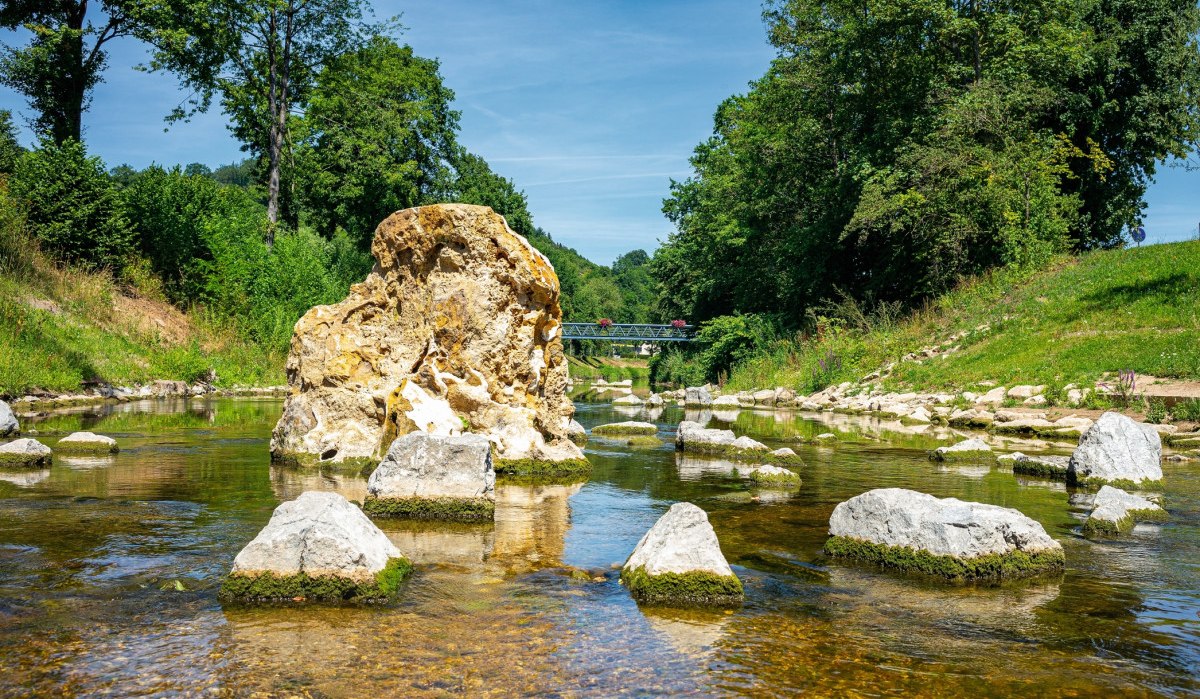 Ein Fluss mit großen Steinen im Wasser, umgeben von grüner Vegetation. Im Hintergrund ist eine Brücke zu sehen., © Remstal Tourismus e.V. Ein Fluss mit großen Steinen im Wasser, umgeben von grüner Vegetation. Im Hintergrund ist eine Brücke zu sehen., © Remstal Tourismus e.V.