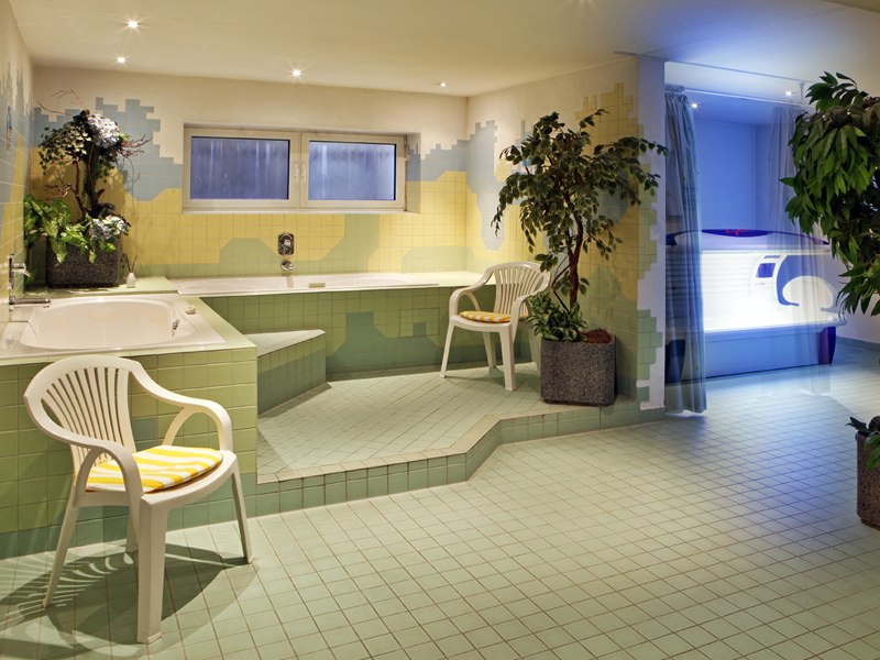 Ein Wellnessbereich mit Whirlpool, Solarium, grünen Fliesen und Pflanzen. Zwei weiße Plastikstühle mit gelben Kissen stehen bereit., © © H-Hotels.com