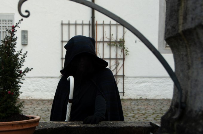 Vermummte Gestalt mit Kapuze und weißem Stock vor einem Brunnen in einem gepflasterten Hof., © Stadt Waldenbuch