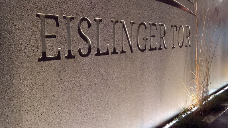 Beleuchtete Steinwand mit der Aufschrift 'Eislinger Tor' und dekorativen Linien. Pflanzen am Boden entlang der Wand., © Hotel Eislinger Tor