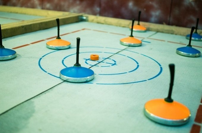 Eisstöcke in Blau und Orange liegen auf einer Zielscheibe beim Eisstockschießen. Der Boden ist markiert und die Stöcke sind verteilt., © Cool-Tours StattReisen