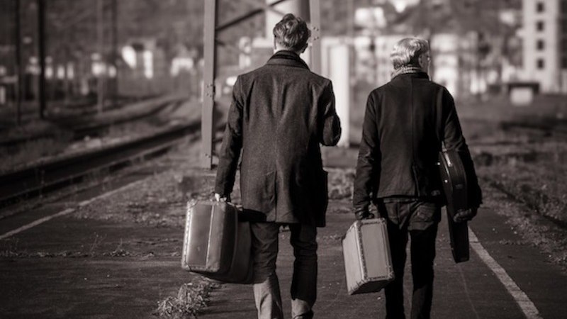Zwei Personen gehen mit Koffern auf einem leeren Bahnsteig. Die Szene ist in Schwarz-Weiß gehalten, was eine nostalgische Stimmung erzeugt., © richtungdichtung Zwei Personen gehen mit Koffern auf einem leeren Bahnsteig. Die Szene ist in Schwarz-Weiß gehalten, was eine nostalgische Stimmung erzeugt., © richtungdichtung