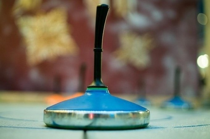 Nahaufnahme eines blauen Eisstocks auf einer Eisbahn, unscharfer Hintergrund mit winterlichen Dekorationen., &copy; Cool-Tours StattReisen